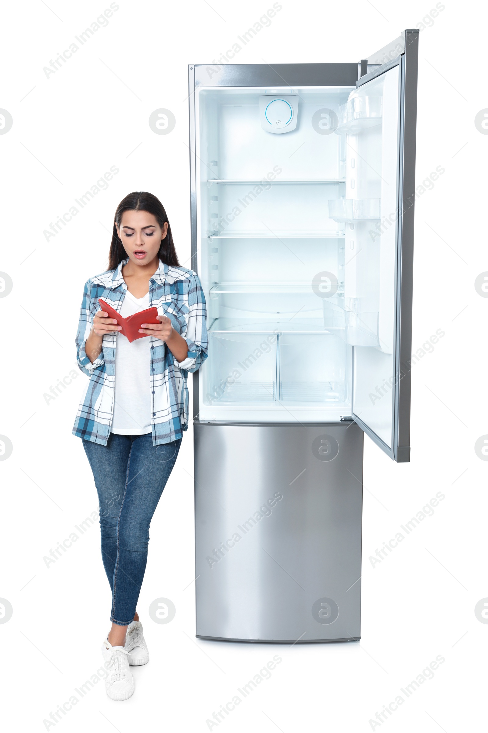 Photo of Young woman with no money in wallet near empty refrigerator on white background