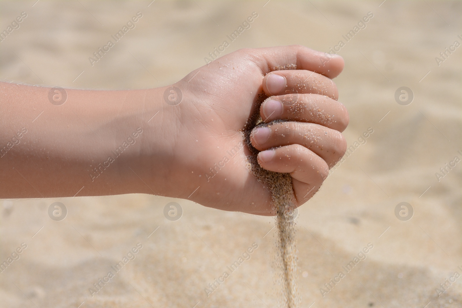 Photo of Child pouring sand from hand outdoors, closeup. Fleeting time concept