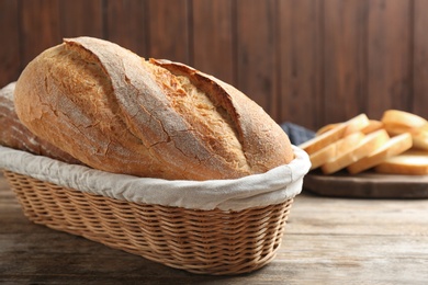 Photo of Loaves of tasty fresh bread in wicker basket on wooden table