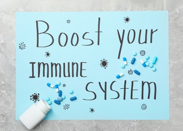 Sheet of paper with words Boost Your Immune System and pills on light grey table, flat lay