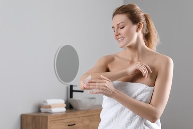 Photo of Happy woman applying body cream onto elbow in bathroom, space for text