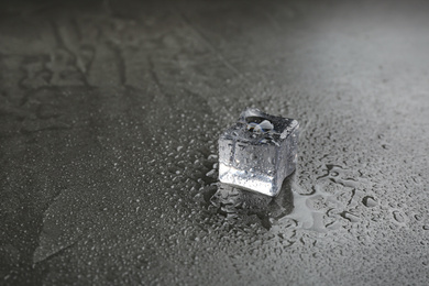 Photo of Crystal clear ice cube on grey stone table. Space for text