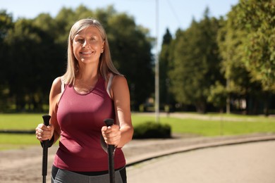 Happy woman with poles for Nordic walking in park on sunny day, space for text