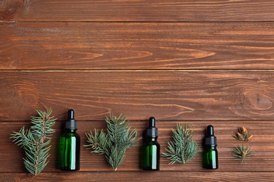 Little bottles with essential oils among pine branches on wooden background, flat lay. Space for text