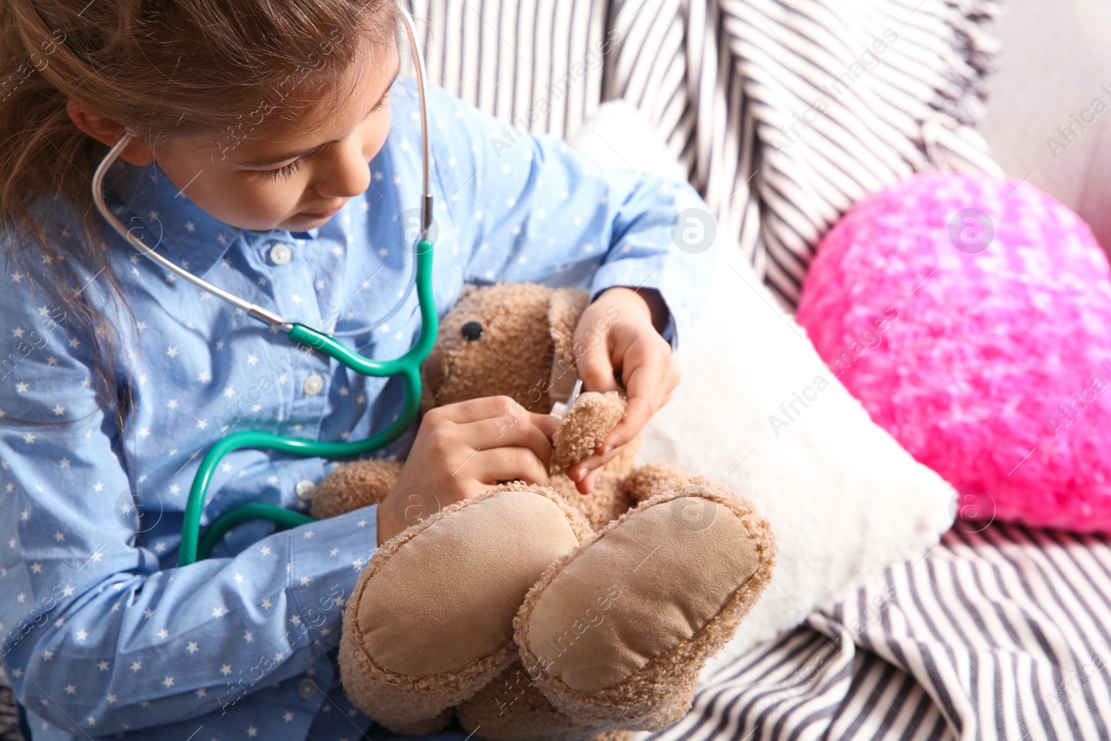 Photo of Cute child imagining herself doctor while playing with stethoscope on sofa in living room