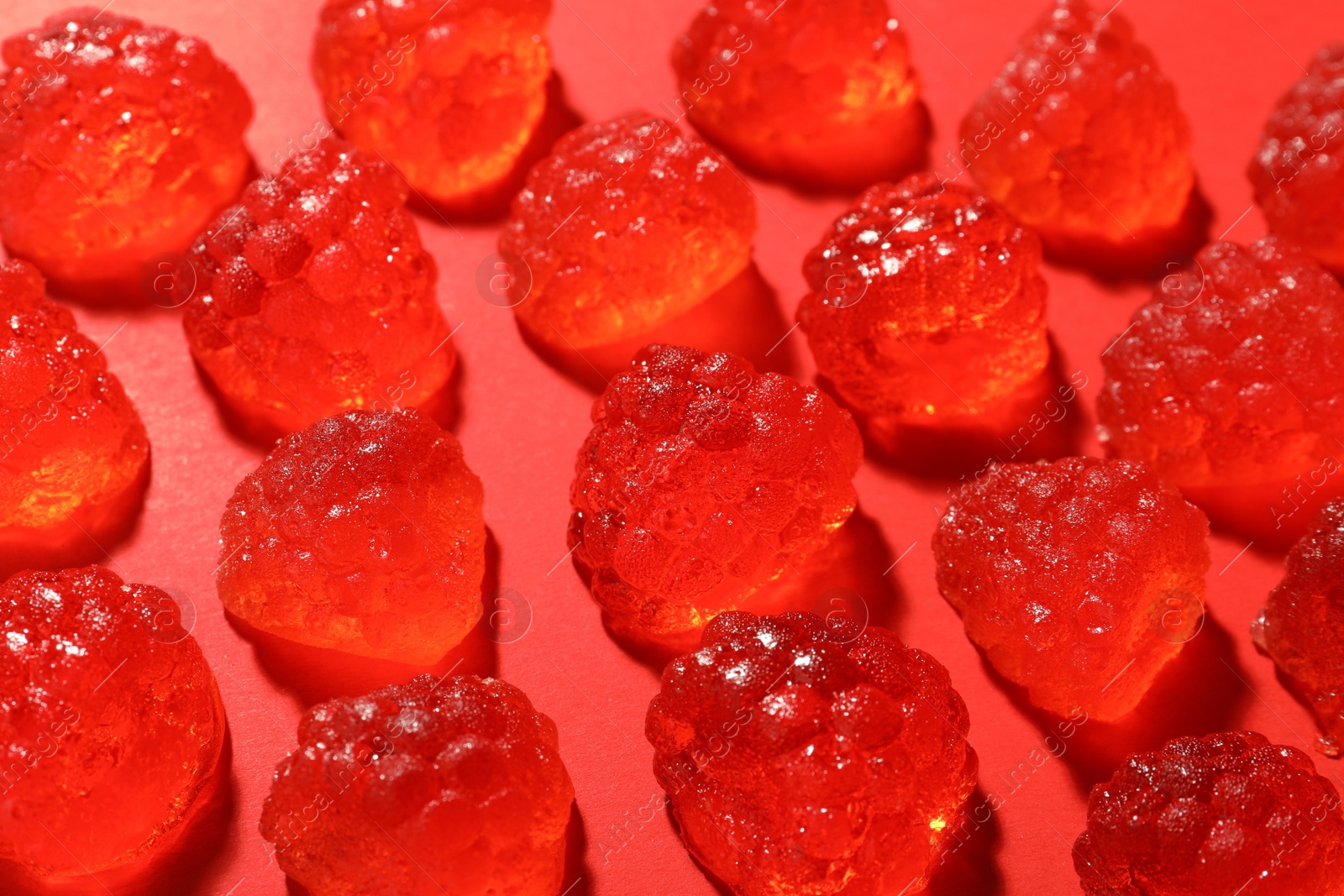 Photo of Delicious gummy raspberry candies on red background, closeup