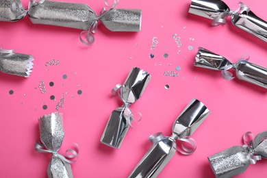 Open and closed silver Christmas crackers with shiny confetti on pink background, flat lay