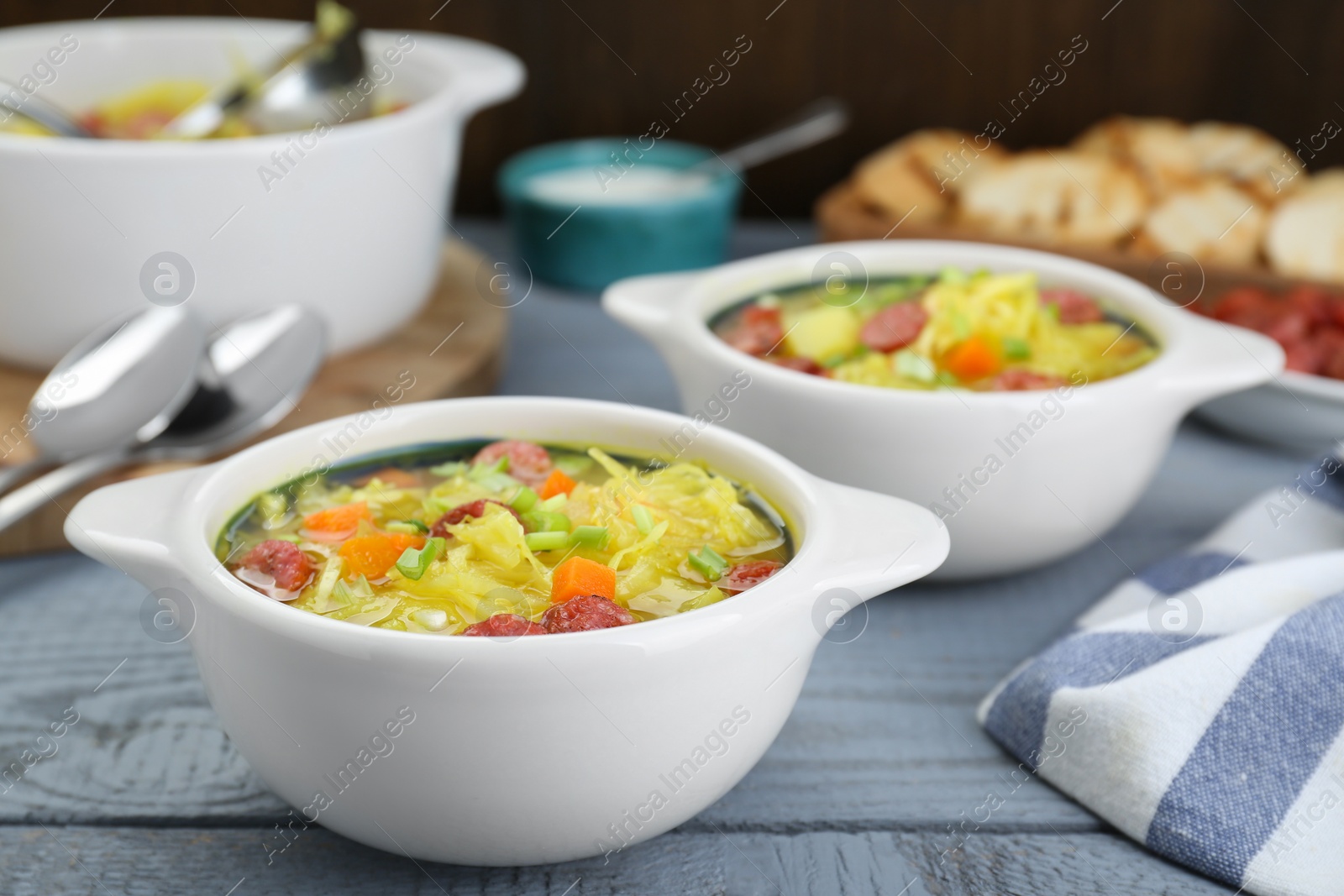 Photo of Delicious sauerkraut soup with smoked sausages and green onion on grey wooden table