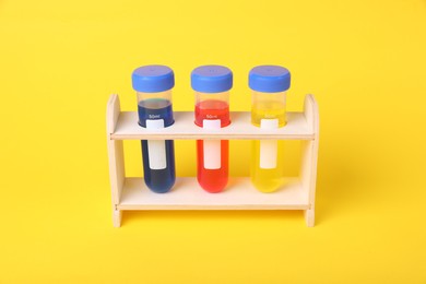 Photo of Test tubes with colorful liquids in wooden stand on yellow background. Kids chemical experiment set