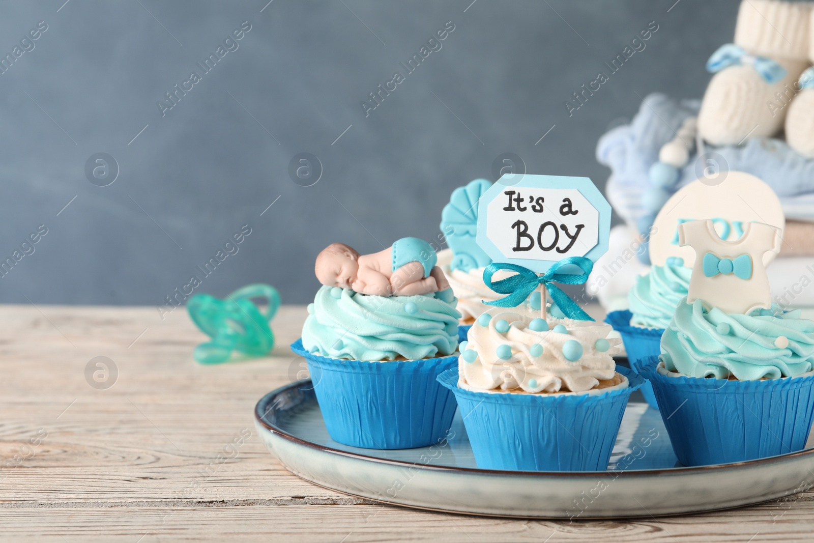 Photo of Beautifully decorated baby shower cupcakes for boy with cream on white wooden table. Space for text