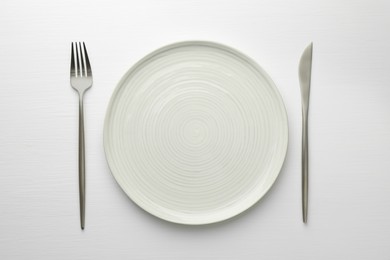 Photo of Empty plate, fork and knife on white table, top view