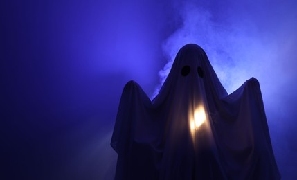 Photo of Creepy ghost. Woman covered with sheet in blue light, space for text