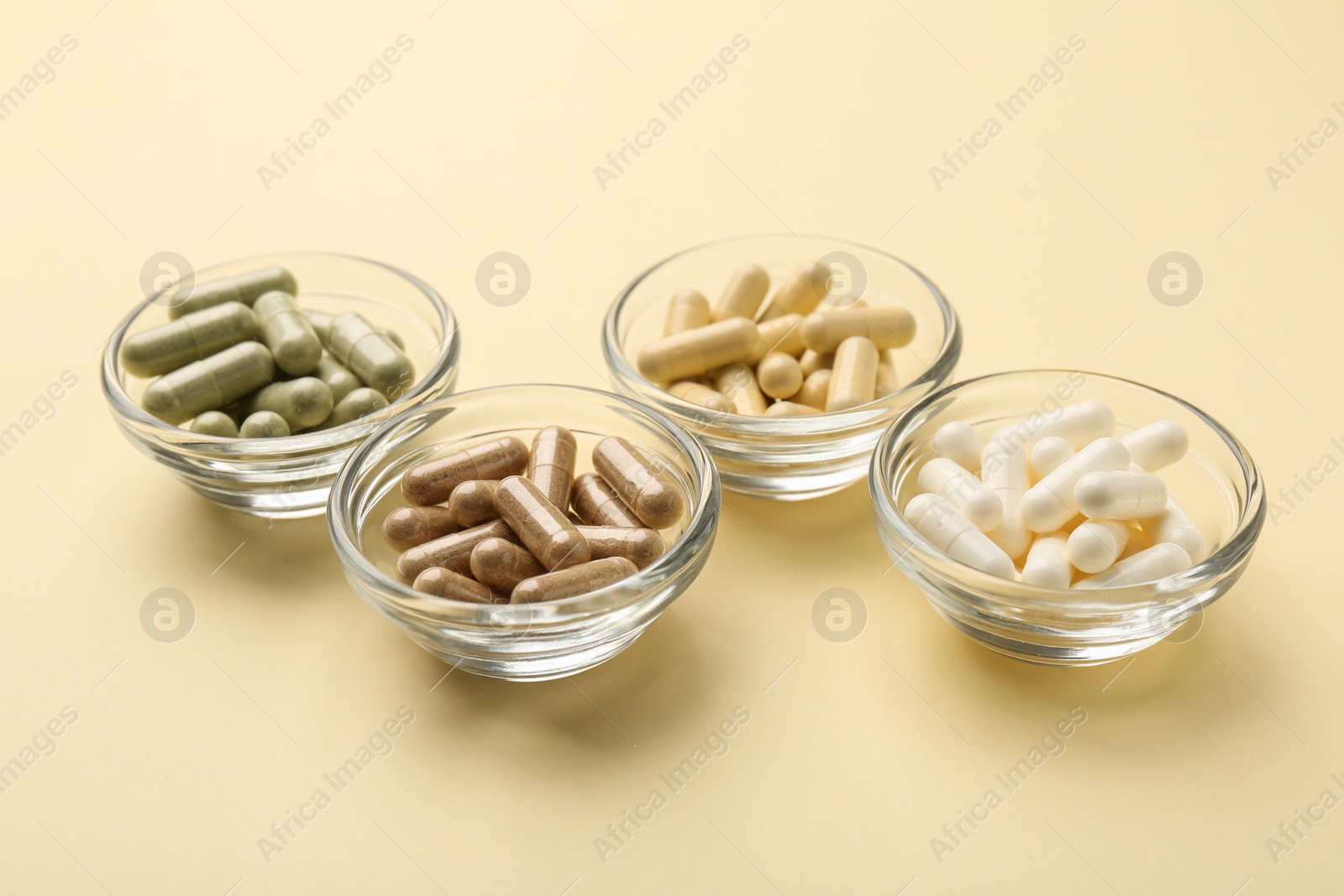 Photo of Different vitamin capsules in bowls on pale yellow background