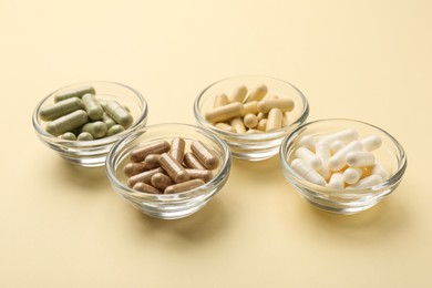 Different vitamin capsules in bowls on pale yellow background