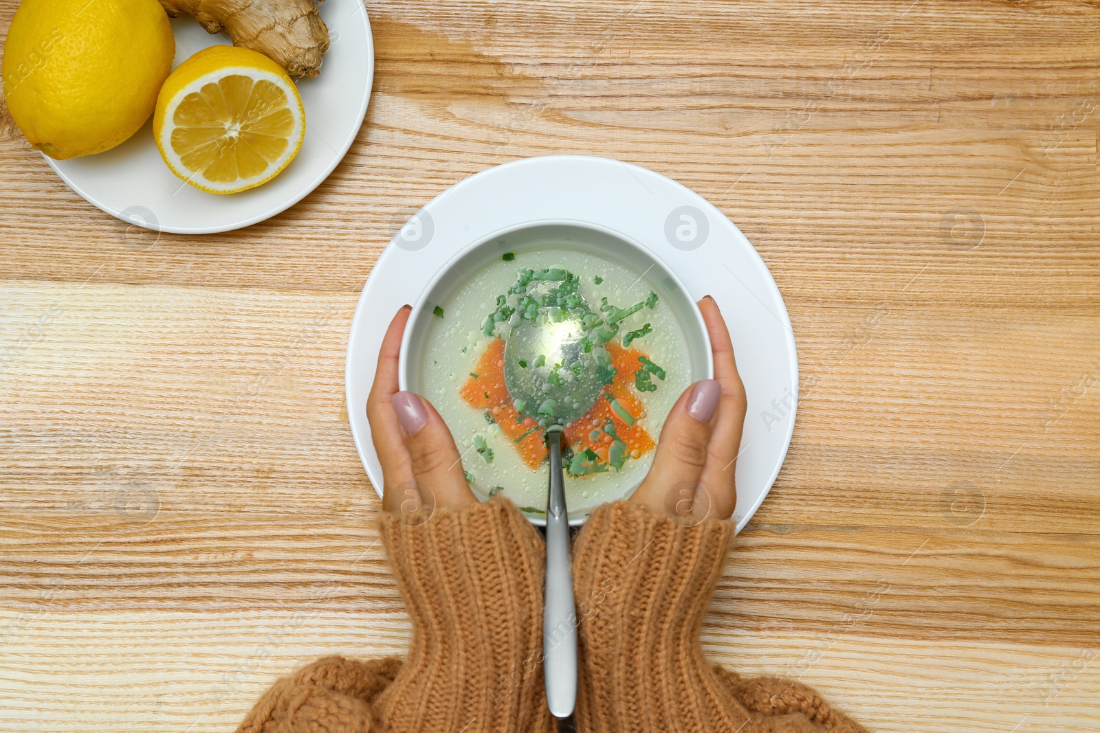 Photo of Woman with bowl of soup at wooden table, top view. Flu treatment