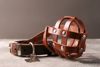 Photo of Brown leather dog muzzle and collar on light gray textured table, closeup