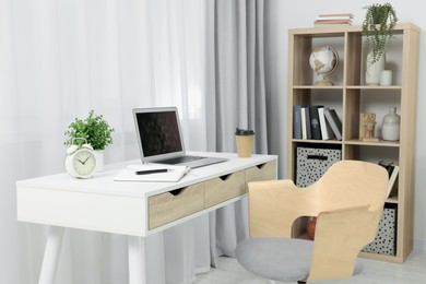Photo of Workplace with modern laptop on desk and comfortable chair at home