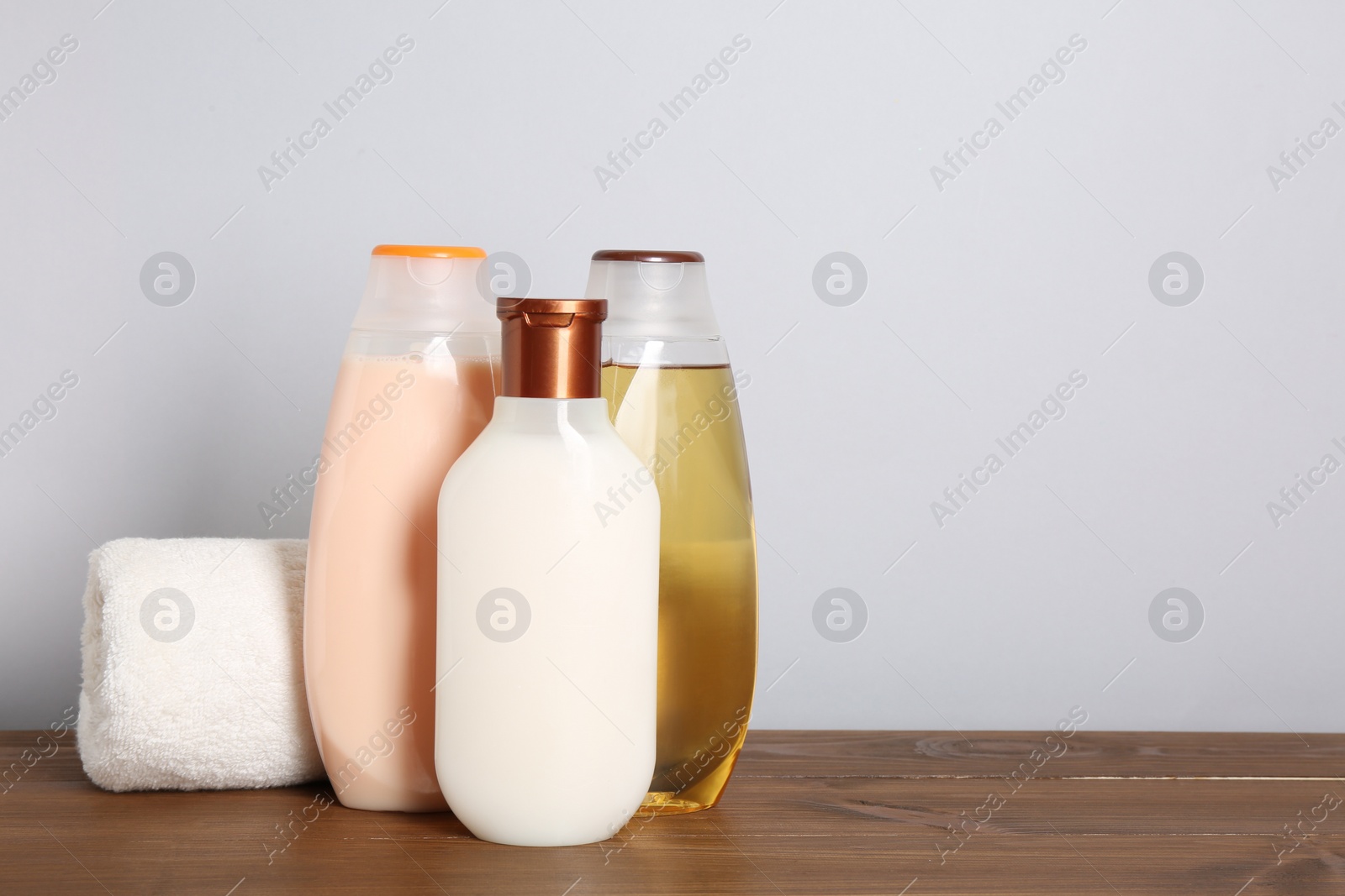 Photo of Different shower gel bottles with towel on wooden table. Space for text