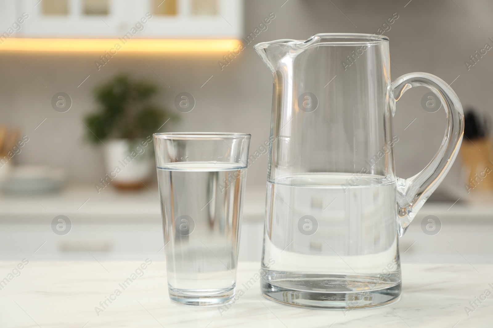 Photo of Jug and glass with clear water on white table in kitchen, closeup