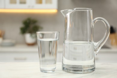 Jug and glass with clear water on white table in kitchen, closeup