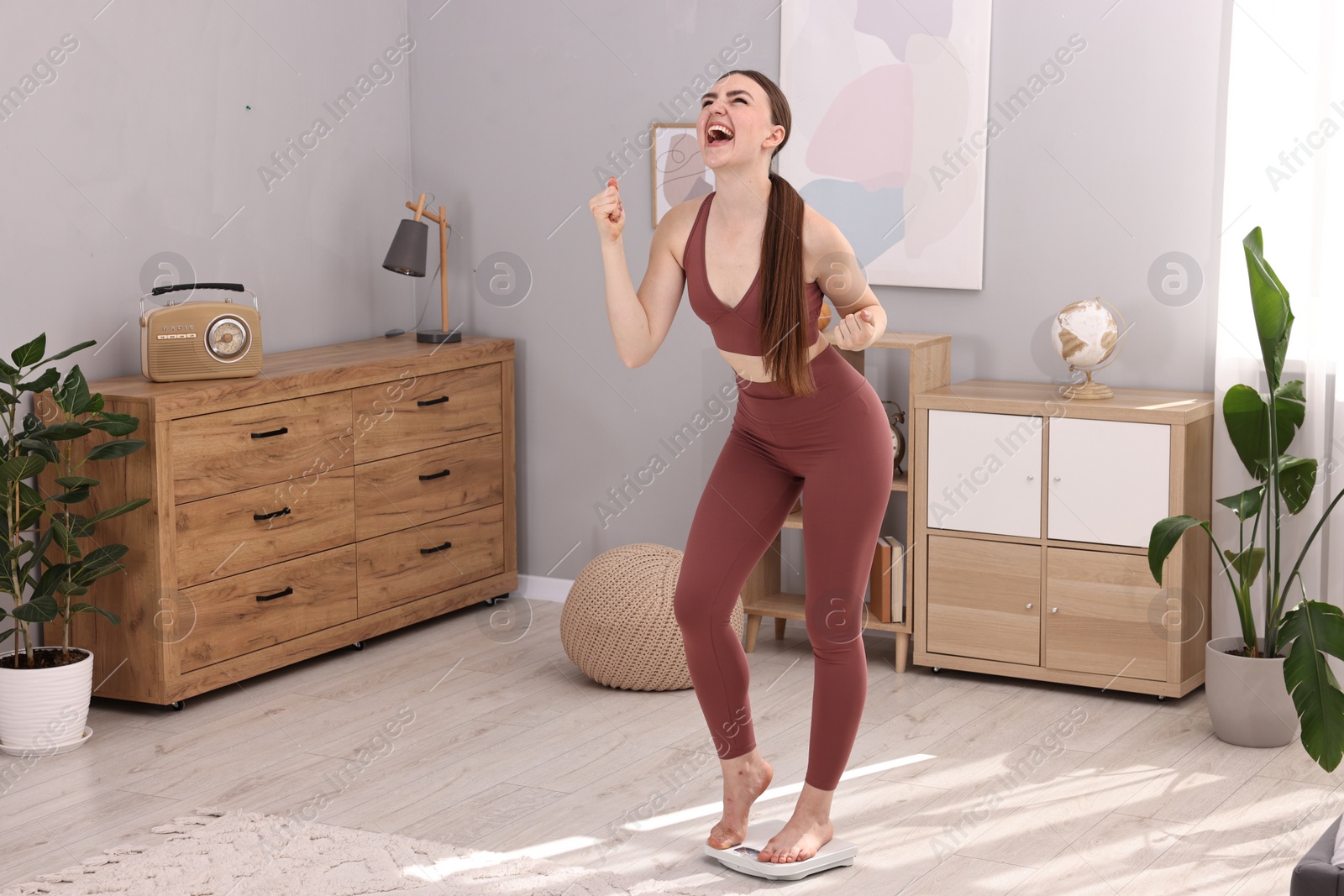 Photo of Happy woman standing on floor scale at home