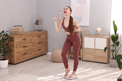 Photo of Happy woman standing on floor scale at home