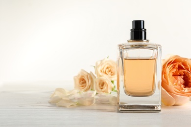 Photo of Elegant bottle of perfume and flowers on light background, space for text