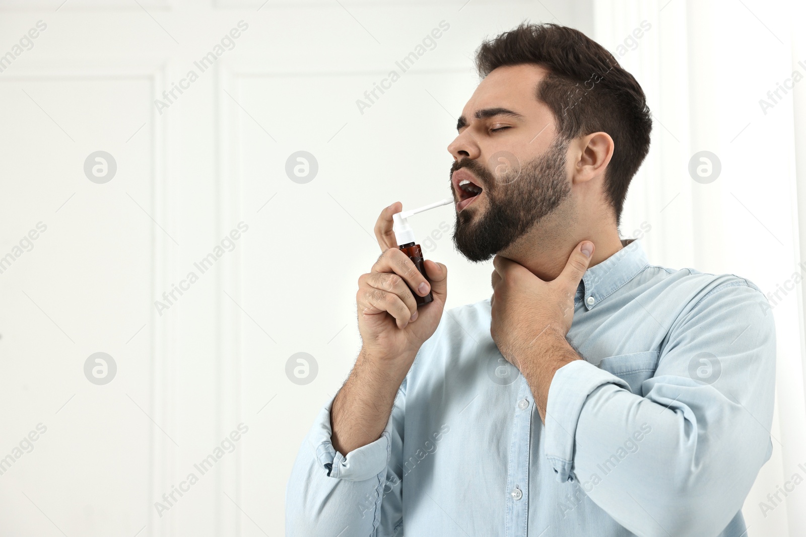 Photo of Young man using throat spray indoors. Space for text