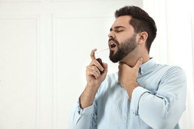 Young man using throat spray indoors. Space for text