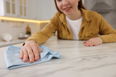 Woman with microfiber cloth cleaning white marble table in kitchen, selective focus
