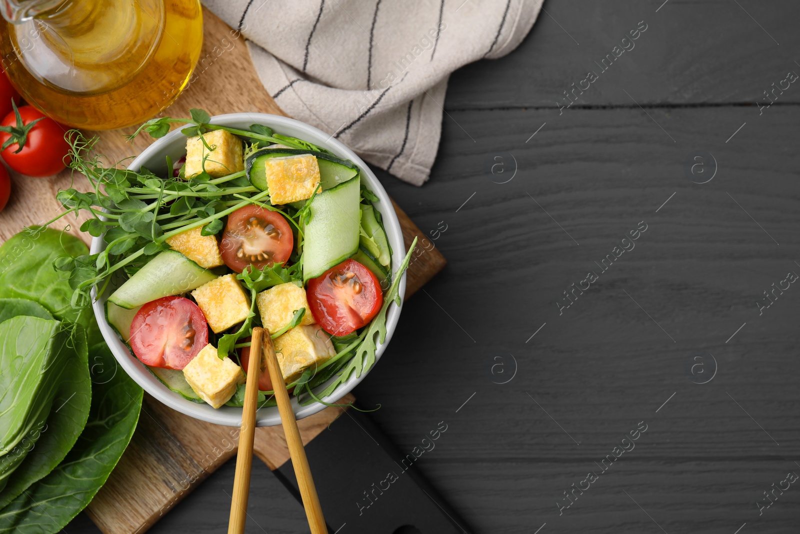 Photo of Tasty salad with tofu and vegetables near ingredients on grey wooden table, flat lay. Space for text