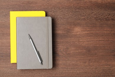 Photo of Stylish notebooks and pen on wooden table, top view. Space for text