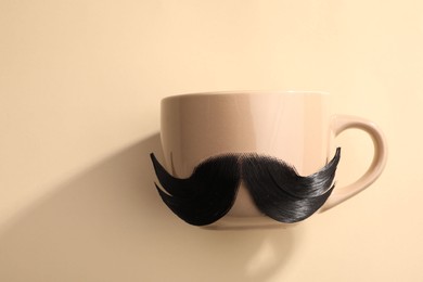Photo of Artificial moustache and cup on beige background, top view