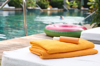 Photo of Beach towels and sunscreen on sun lounger near outdoor swimming pool, selective focus. Luxury resort