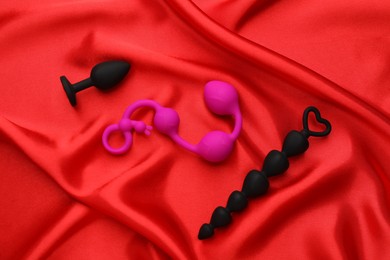 Photo of Sex toys on red fabric, flat lay
