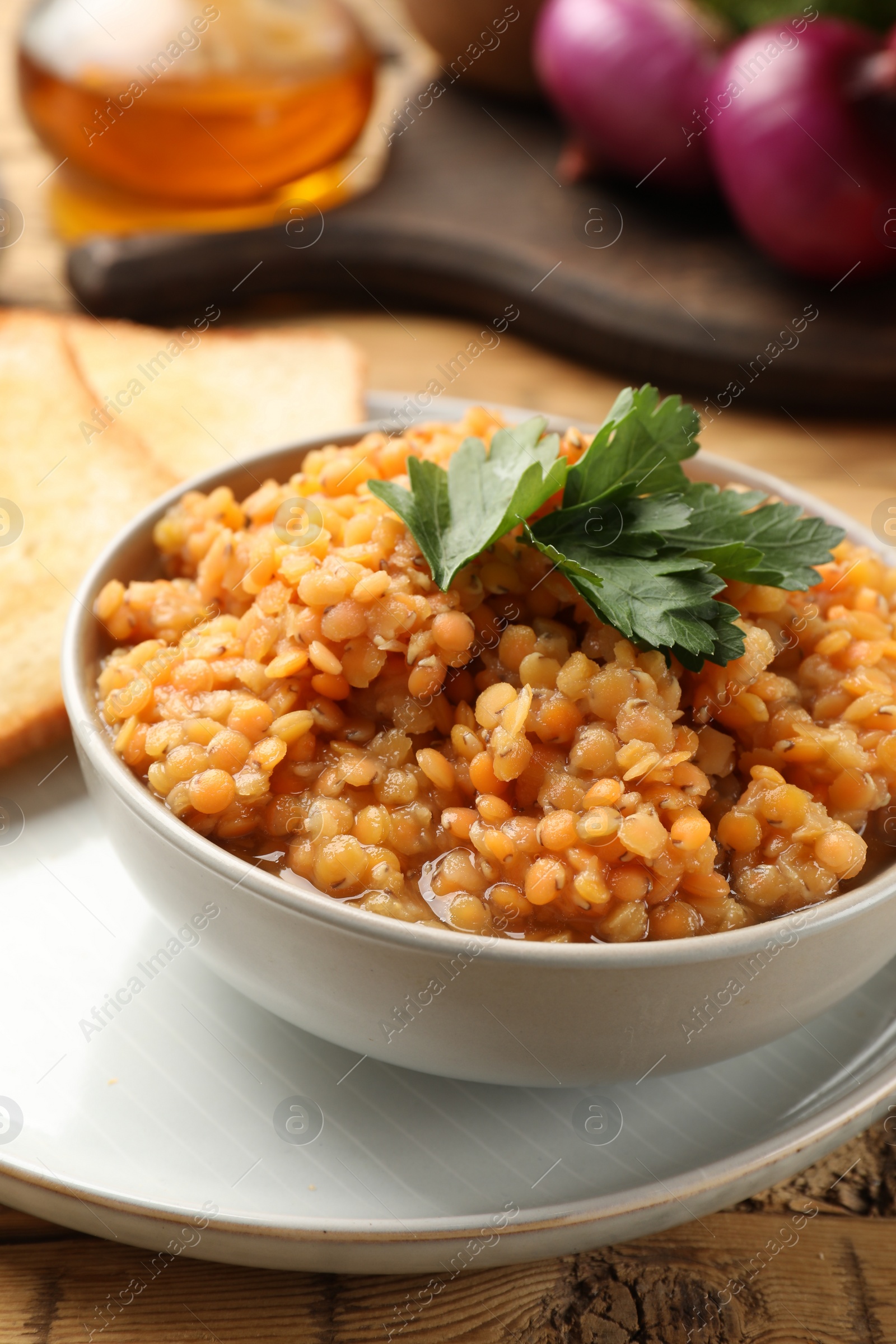 Photo of Delicious red lentils with parsley in bowl served on table, closeup