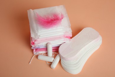 Photo of Menstrual pads with pink feather and other period products on pale orange background
