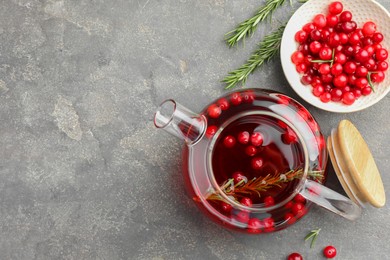 Photo of Tasty hot cranberry tea in teapot, rosemary and fresh berries on light grey textured table