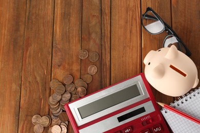 Flat lay composition with calculator, coins and piggy bank on wooden table. Space for text