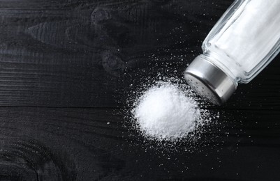 Photo of Organic salt in glass shaker on black wooden table, top view. Space for text