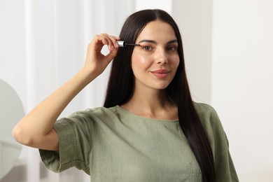 Beautiful woman applying serum onto her eyelashes in room. Cosmetic product