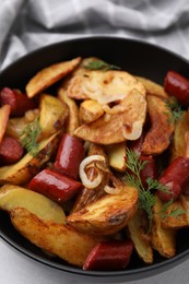 Photo of Delicious baked potato with thin dry smoked sausages, onion and dill in bowl on table, closeup