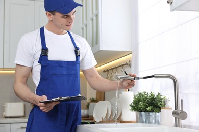 Young plumber with clipboard examining faucet in kitchen