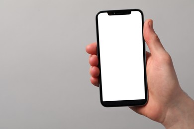 Man holding smartphone with blank screen on light grey background, closeup. Mockup for design