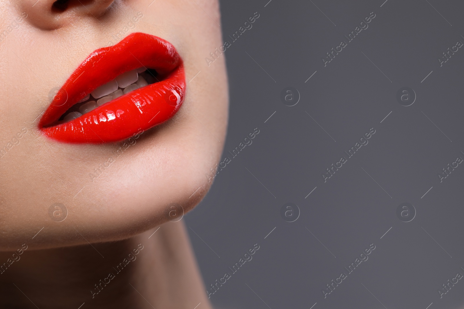 Photo of Young woman with beautiful red lips on grey background, closeup. Space for text