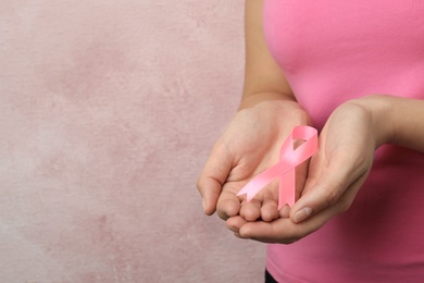 Photo of Woman holding pink ribbon on color background, closeup with space for text. Breast cancer awareness