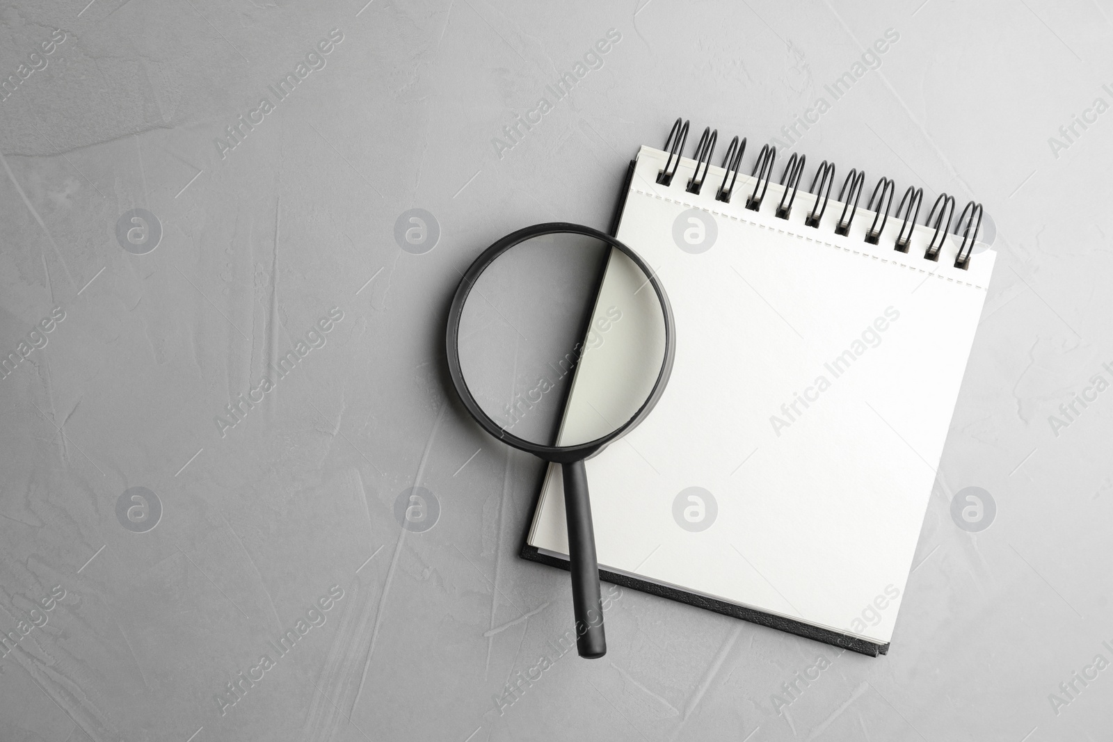 Photo of Top view of magnifier glass and empty notebook on light grey stone background, space for text. Find keywords concept