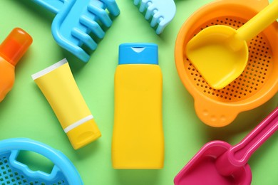 Bottle of suntan cream and children's beach toys on green background, flat lay