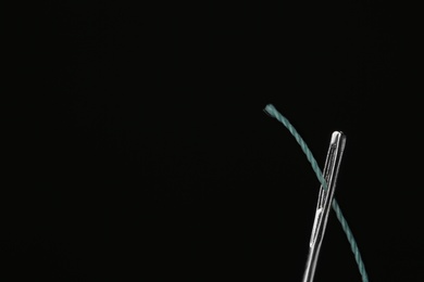 Photo of Needle with sewing thread on black background, closeup