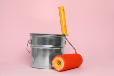 Can of orange paint and roller on pink background